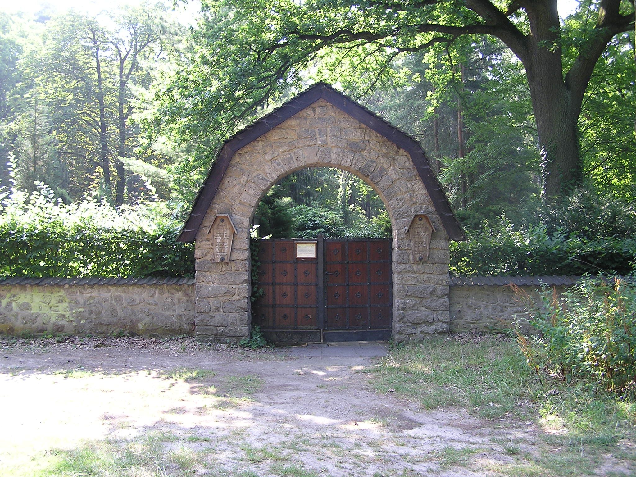 Steinernes Eingangsportal des Friedhofs Grunewald-Forst zwischen hohen Bäumen